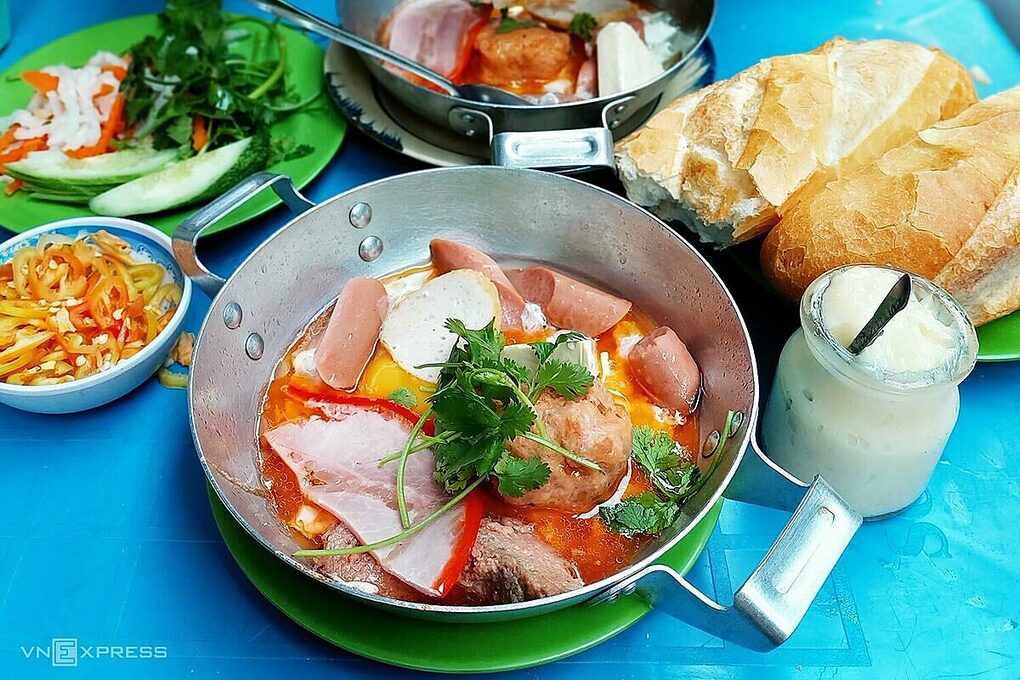 Bánh mì chảo với phần trứng chiên lòng đào, pate, chả lụa, jambon, xúc xích, phô mai và viên xíu mại mềm không bị khô là món sáng nhiều năng lượng cho thực khách. Ổ bánh mì giòn xé nhỏ chấm với nước sốt đậm đà trong chảo bánh mì lúc nóng, ăn kèm đồ chua, dưa leo cắt miếng mỏng, ngò rí cùng các loại gia vị nêm nếm vừa miệng theo khẩu vị. Quán nằm trong hẻm Đặng Trần Côn trên đường